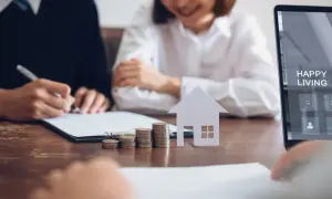 Para podpisania wniosku o wpis hipoteki na rzecz banku. Stół z dokumentami, monetami, domkiem i ekranem laptopa z napisem "Happy Living".