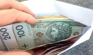 Dłoń wsuwa kopertę z banknotami 100 i 200 zł. Zastanawiasz się, renta wdowia komu przysługuje?