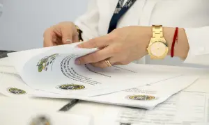 Dłonie przeglądają dokumenty, wśród których znajdują się oświadczenia o poddaniu się egzekucji. Złoty zegarek i czerwona nitka na nadgarstku.