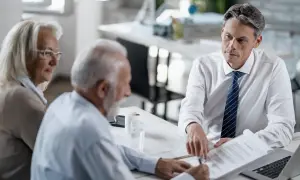 Starszy mężczyzna i kobieta omawiają dokumenty z prawnikiem. Prawdopodobnie chodzi o akt poświadczenia dziedziczenia i potrzebne dokumenty.