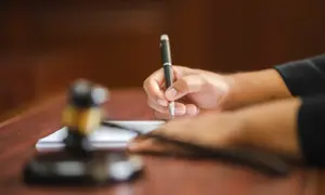 Dłoń pisze piórem na papierze, obok młotek sędziowski. Tak pracuje referendarz sądowy, kto to?