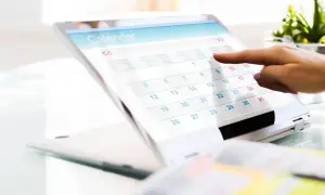 Palec wskazuje datę na ekranie tabletu z kalendarzem. Planowanie urlopu i świadczenie urlopowe to ważne kwestie.
