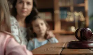 Matka, jako przedstawiciel ustawowy dziecka, w sądzie. Obok młotek sędziowski i waga sprawiedliwości.