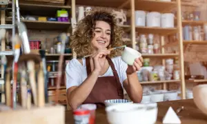 Uśmiechnięta artystka maluje ceramikę w swojej pracowni. To miejsce, gdzie powstaje i sprzedawana jest produkcja i sprzedaż rękodzieła pkd.