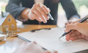 Podpisanie umowy najmu. Dwie osoby przy stole, jedna wskazuje na dokument, druga podpisuje. Obok model domu. Kiedy wypowiedzenie umowy najmu jest bezskuteczne.