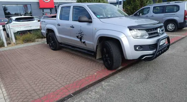 Srebrny pickup z naklejką kompasu i postacią, gotowy do podróży. Idealny do pkd wynajem samochodów.