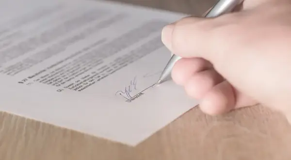 Podpisanie umowy kupna sprzedaży domu. Dłoń z długopisem składa podpis na dokumencie.