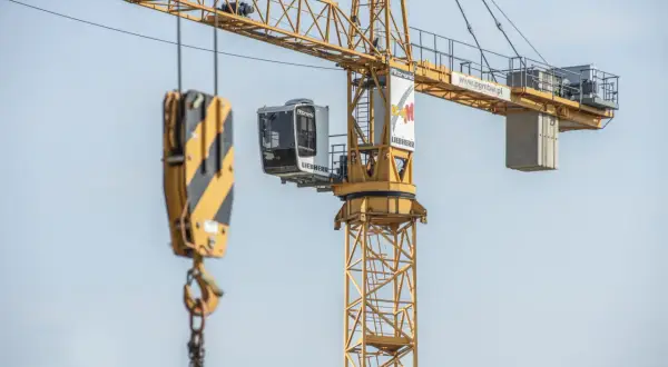 Kabina operatora żurawia wieżowego Liebherr, z widocznym hakiem i łańcuchami, gotowa do pracy na budowie.