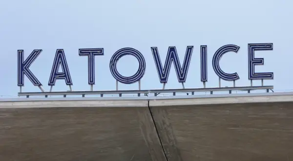 Napis KATOWICE z niebieskimi neonami na tle błękitnego nieba.