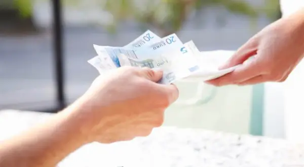 Dwie dłonie przekazują sobie banknoty euro. Jedna ręka podaje pieniądze, druga odbiera. To transakcja, która pokazuje, na poczet czego jest płatność.