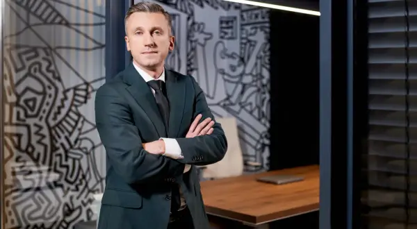 Mężczyzna w garniturze stoi z rękami skrzyżowanymi na piersi w nowoczesnym biurze.