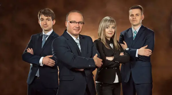 Cztery osoby w garniturach stoją ze skrzyżowanymi rękami na tle brązowym.