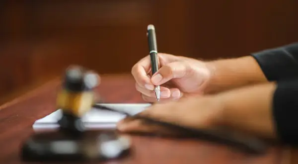 Dłoń pisze piórem na papierze, obok młotek sędziowski. Tak pracuje referendarz sądowy, kto to?