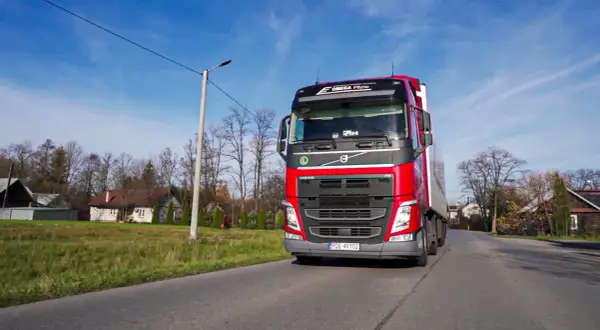 Czerwona ciężarówka Volvo z naczepą jedzie drogą. To praca spedytora, kod zawodu 334101.