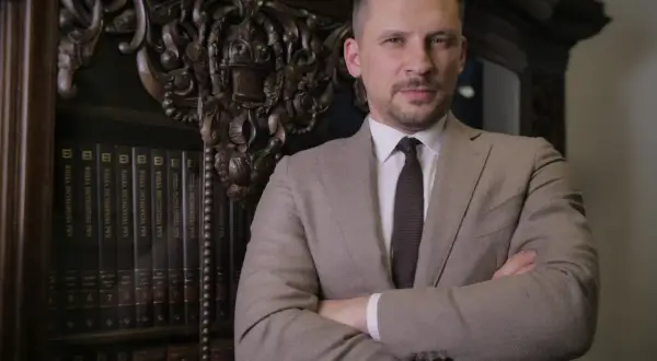 Mężczyzna w garniturze stoi przed regałem z książkami.