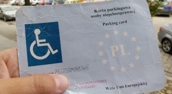 Karta parkingowa osoby niepełnosprawnej z symbolem wózka inwalidzkiego i napisem "PL". Umożliwia korzystanie z miejsca parkingowego dla osób niepełnosprawnych.