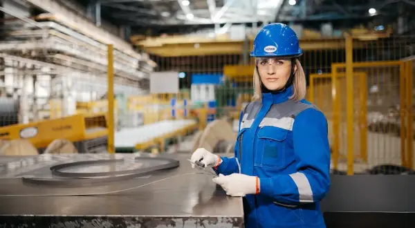 Kobieta w niebieskim kasku i okularach ochronnych, pracująca w hali produkcyjnej. Dba o BHP, co to znaczy? Bezpieczeństwo i higiena pracy.