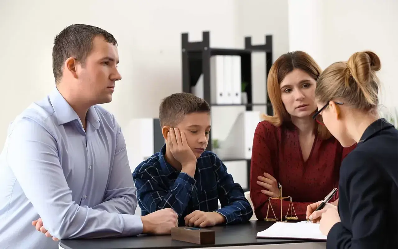 Rodzina z synem rozmawia z prawniczką, która wyjaśnia, co to kurator. Na stole waga sprawiedliwości.