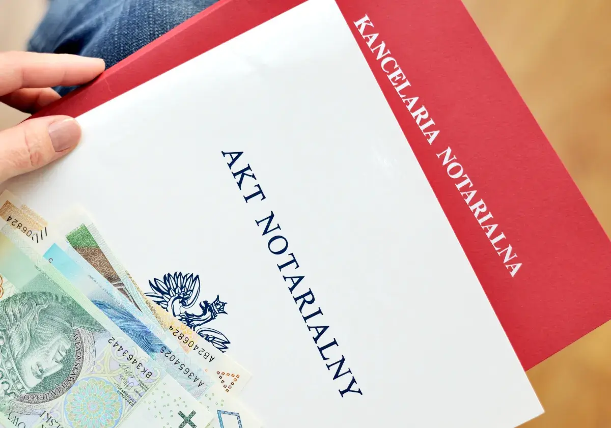 Dłoń trzyma dokument "Akt notarialny" z polskimi banknotami.