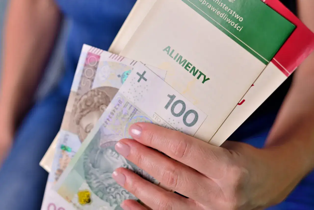 Dłoń trzyma polskie banknoty i dokument z napisem