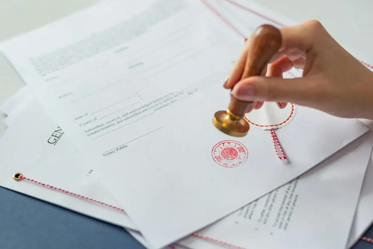 Dłoń z pieczęcią notarialną stempluje dokument. Potwierdzam zgodność z oryginałem.